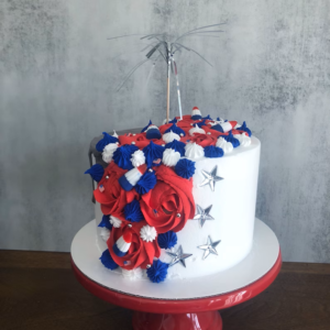 Fake food patriotic cake decorated with silver stars, a drizzle of chocolate, and red, white and blue rosettes