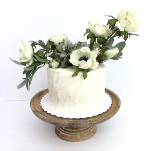 Fake food:  Fake cake with white frosting and decorative white flowers and greenery on the top