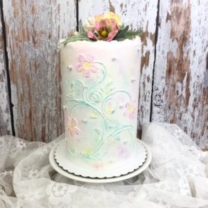 Fake food:  tall fake cake frosted in white with pink flowers and light green stems drawn on the sides.  It's topped with a matching floral arrangement